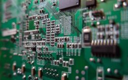 Close-up view of a green printed circuit board (PCB) showcasing surface mount technology (SMT) components such as resistors, capacitors, and integrated circuits, with visible traces and solder joints.