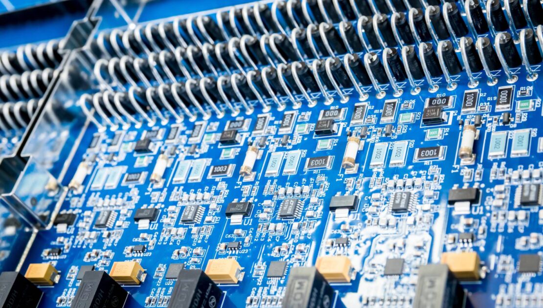 Close-up of a blue printed circuit board assembly with dense surface-mount components and rows of wire-wound elements.