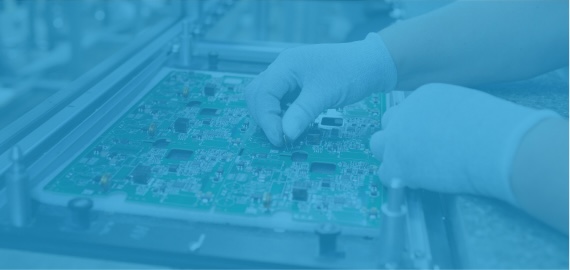 Gloved hands placing a component by hand onto a circuit board held in a production fixture, shown in a light blue tint.