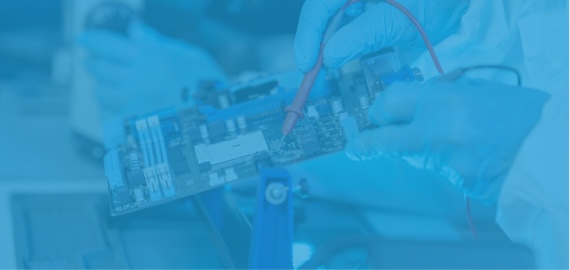 Gloved hands in a cleanroom suit test a circuit board with a multimeter probe.
