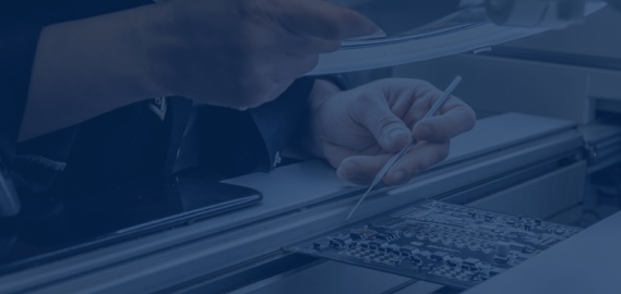 Technician holding a document in one hand and tweezers over a printed circuit board in the other.